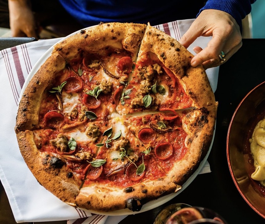 a hand grabbing a slice of pizza with red sauce and sausage