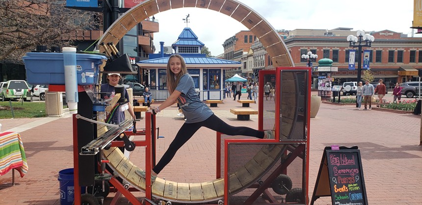 a girl standing in a human-sized hamster wheel