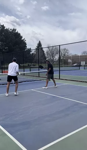 Athletes play pickleball in front of a background of empty tennis courts.