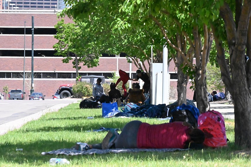 Migrants laying their sleeping bags out under the shade of the trees outside the 5th Street Garage on the Auraria Campus in Denver, Colorado.