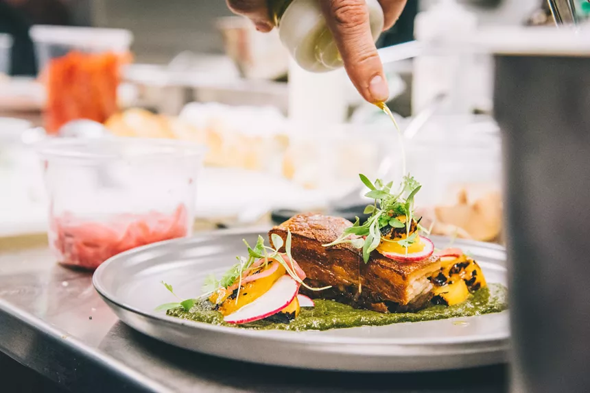oil being poured on a composed plate of food in a kitchen.