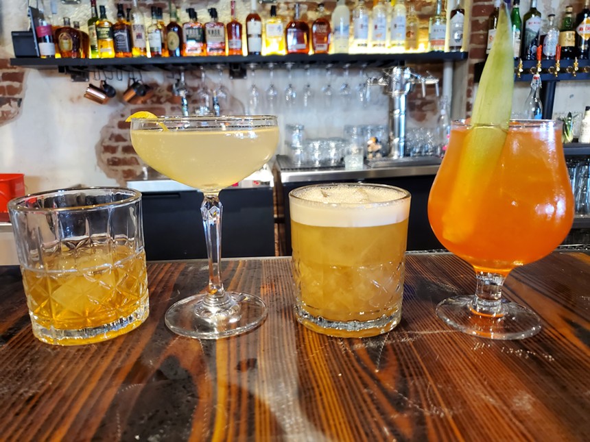 four cocktails lined up on a bar