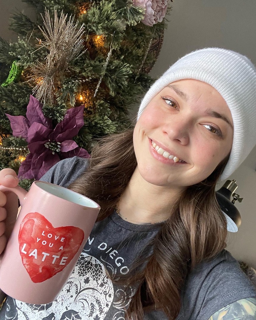 A woman in a white beanie poses with a pink mug.