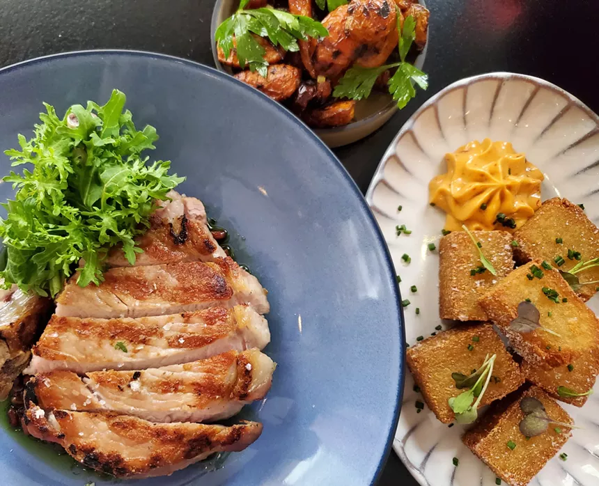 a slicved pork chop next to a bowl of carrots and a plate of fried potatoes