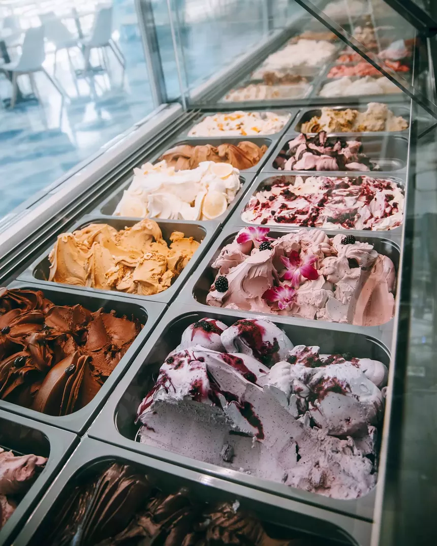 Tubs of different flavored gelato organized next to each other inside of a fridge.
