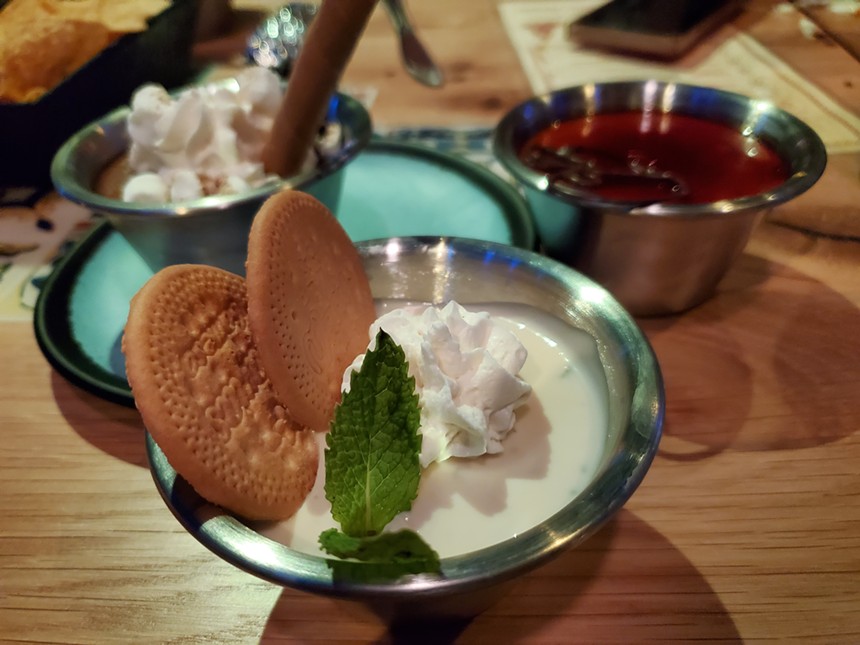 a dessert in a small silver bowl topped with whipped cream, mint and two cookies
