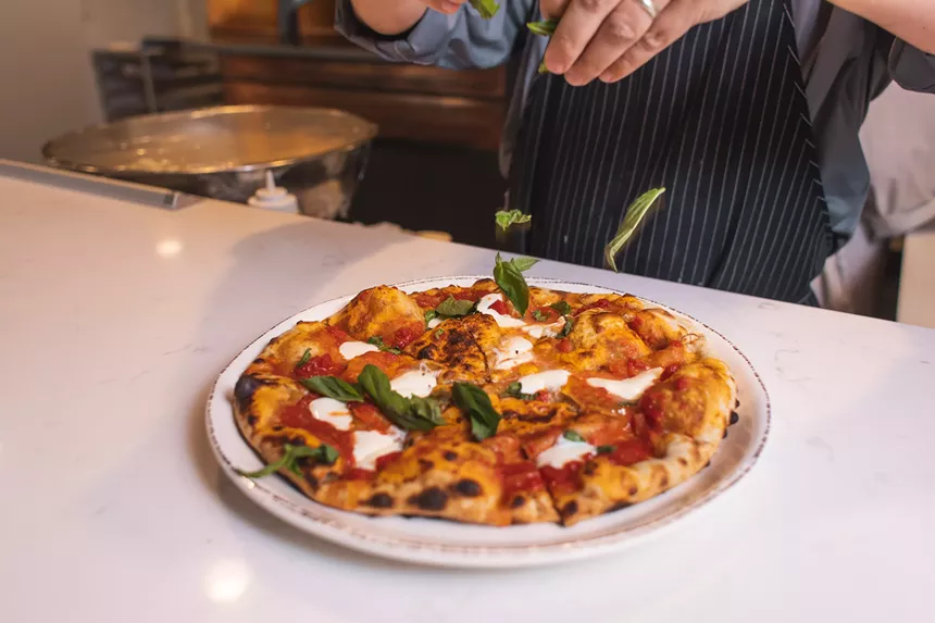 hands sprinkling basil on a pizza