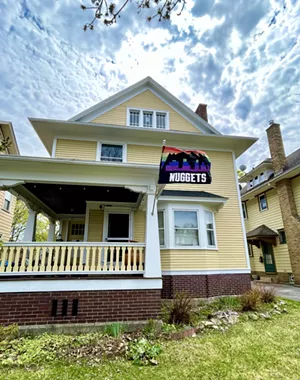 A three-story yellow victorian house with a rainbow Nuggets flag flying on the porch.