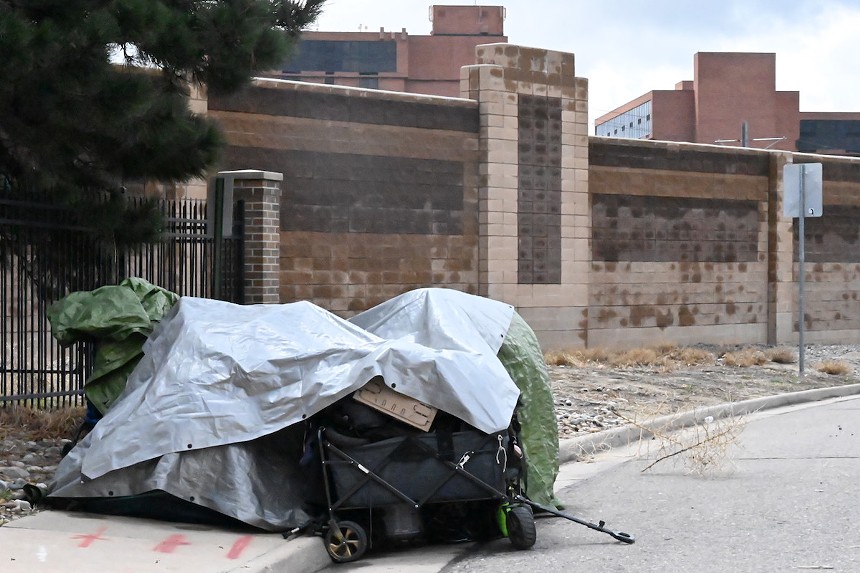 A tent with belongings sits on a residential road in Aurora that runs on the other side of a wall along Interstate 225.