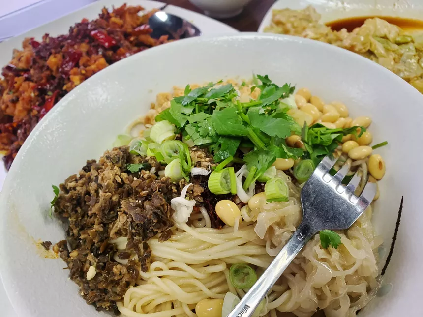 a fork on top of a bowl filled with noodles and herbs