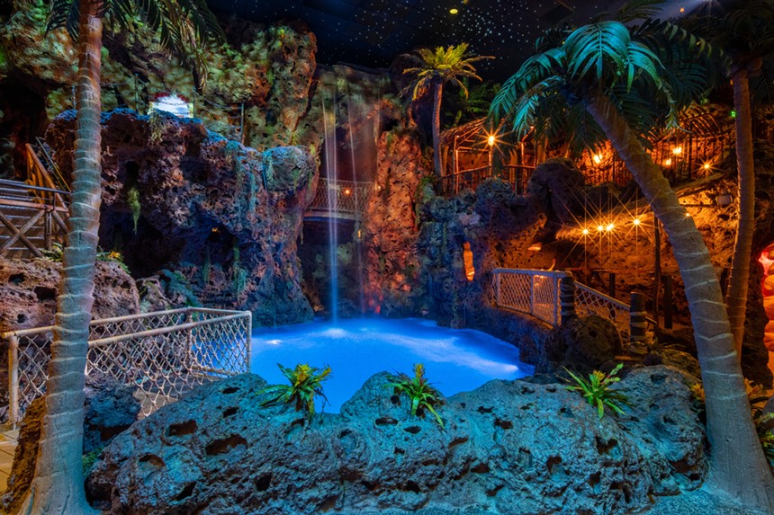 an indoor pool with a waterfall surrounded by cliffs and trees