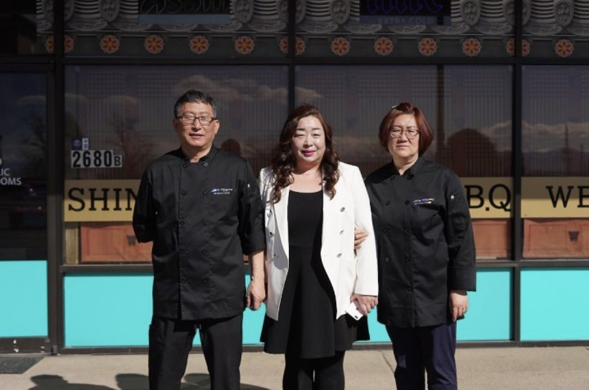two people in black chef's coats with a woman in a white blazer