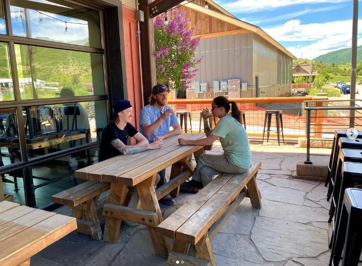 three people sitting at a wooden picnic table on a patio