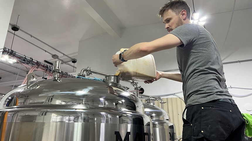 a man pouring a substance into the top of a fermenter