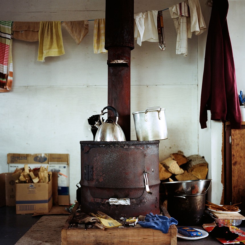 an old fashioned stove with tea kettle, work gloves and timber in the background