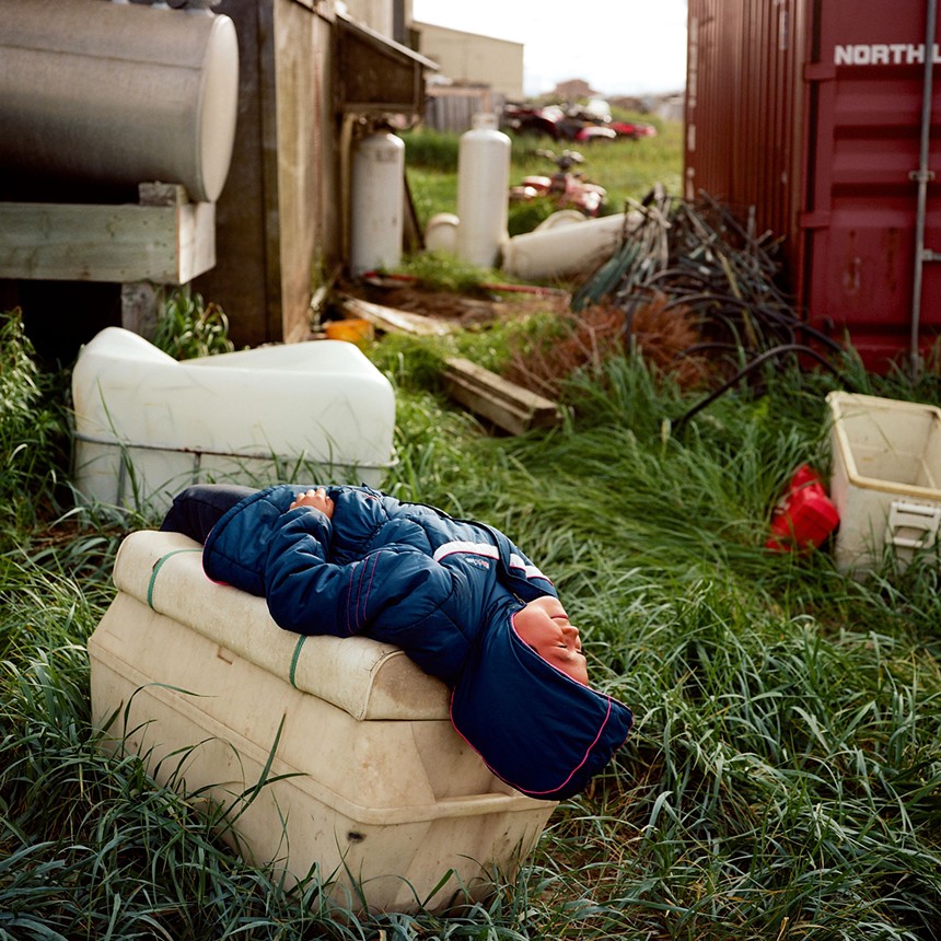 child in a blue jacket resting on a box and looking at the sky surrounded by farm equipment