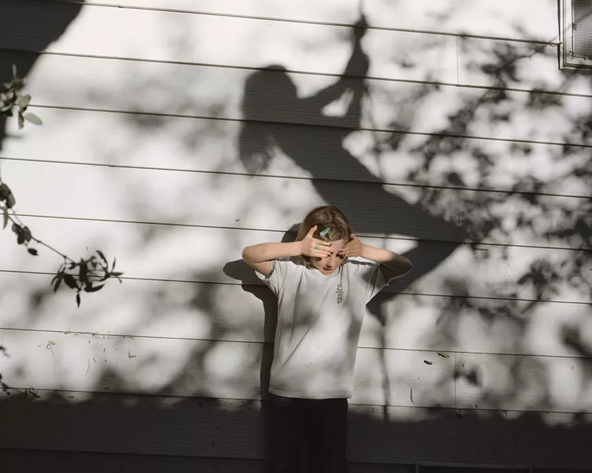 girl covers her eyes with the shadow of a child on a swing behind her