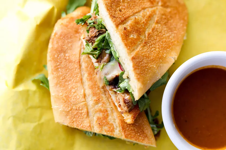 a sandwich next to a bowl of jus