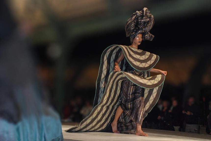 fashion model on the runway in sculptural black and gold dress.