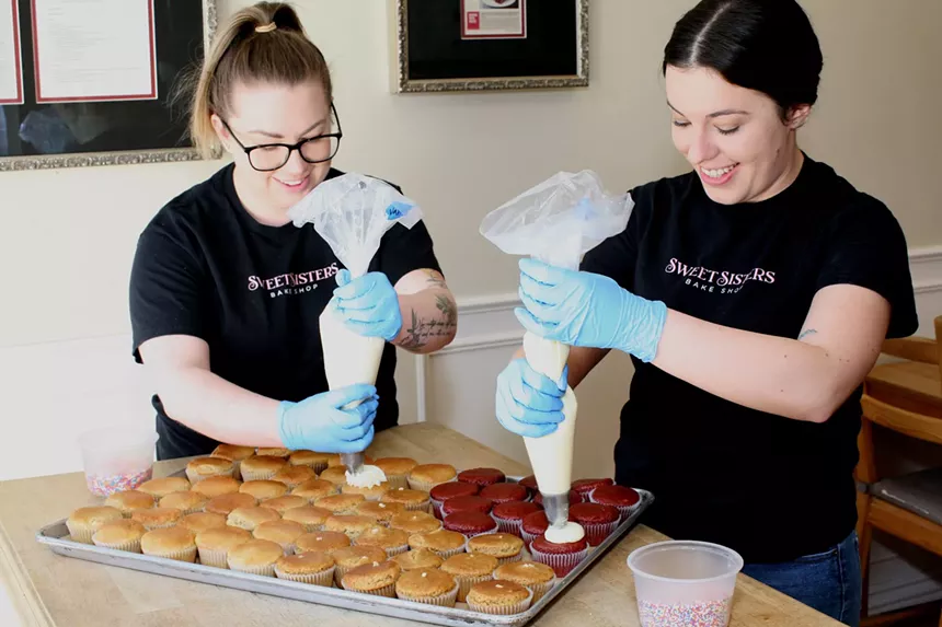 two women holding pastry bags as they decorate cupcakes