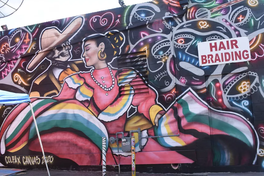 Mural of woman and skeleton dancing, surrounded by colorful, neon skulls.
