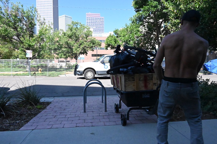 A homeless Denver resident pulls his stuff away from the curb as a Denver Police cruiser passes by.