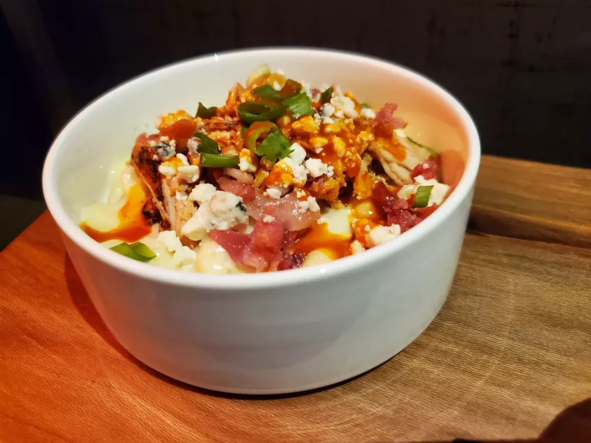a white bowl filled with macaroni topped with chicken and red sauce