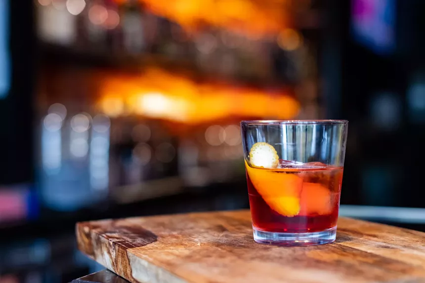 red cocktail sits on wood table