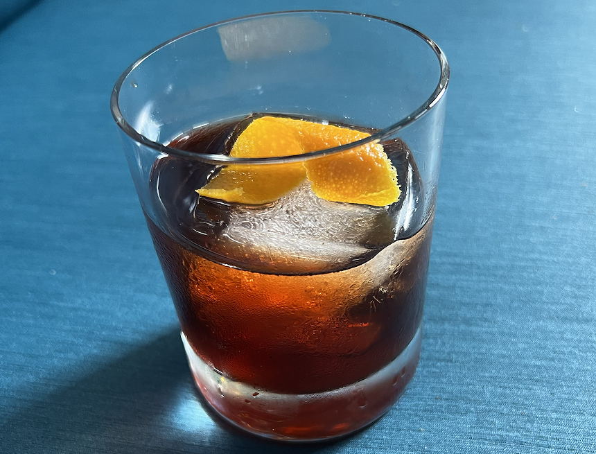 glass of red liquid with orange peel and a blue background