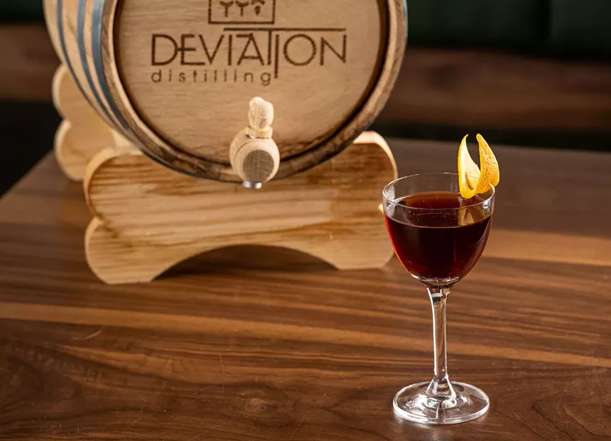 barrel with dark cocktail in front of it on table