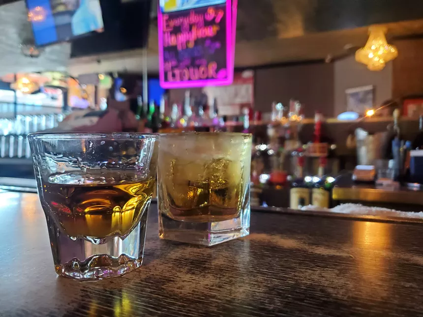 a shot of whiskey next to a cocktail on a bar