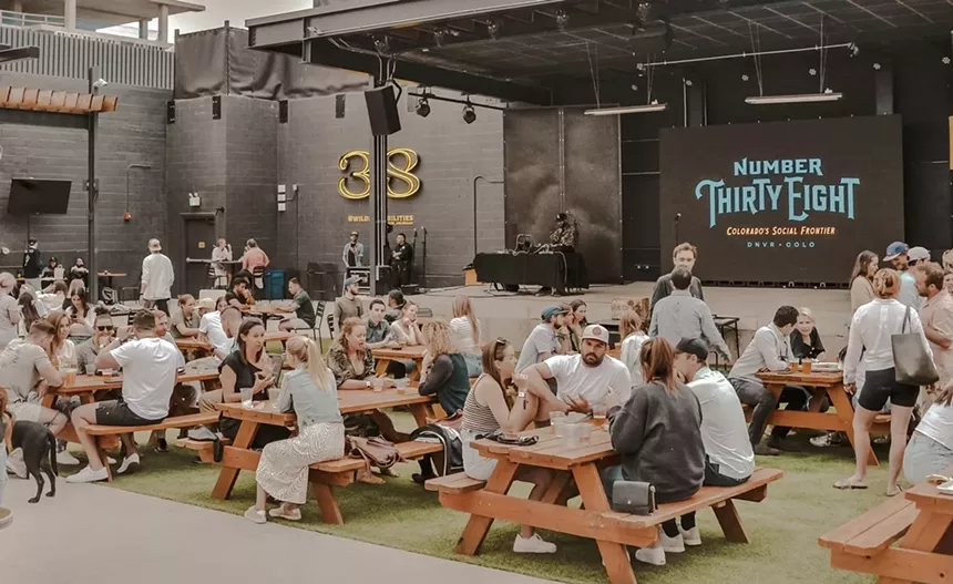 Crowded picnic tables host young people drinking beers.