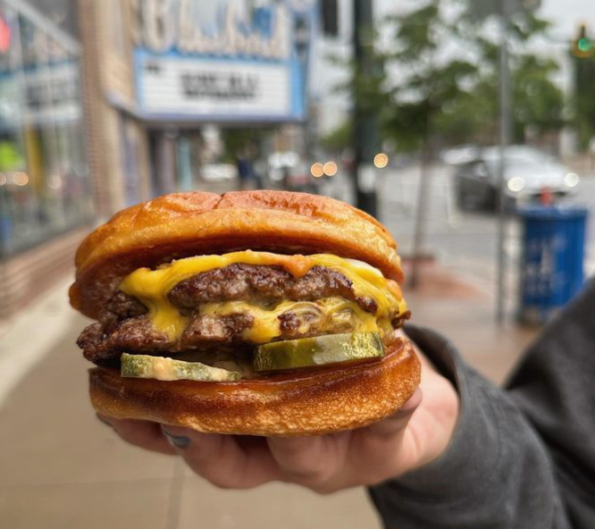 a hand holding a double cheeseburger