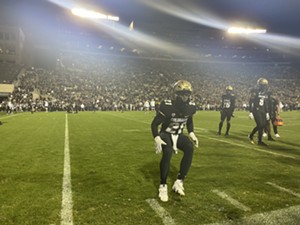 A football player with a gold helmet runs toward the sidelines.