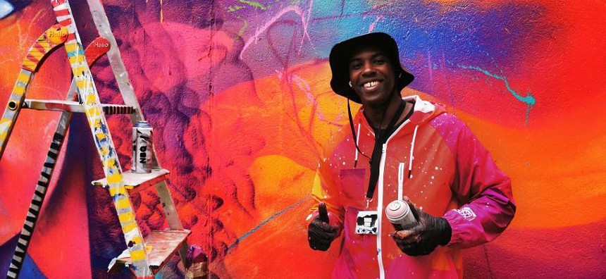 mural artist smiling with a spray paint can giving thumbs up sign