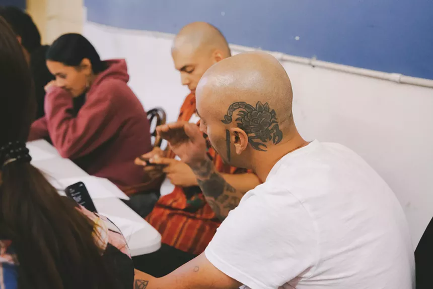 man in white shirt with scorpion tattooed on the side of his head.