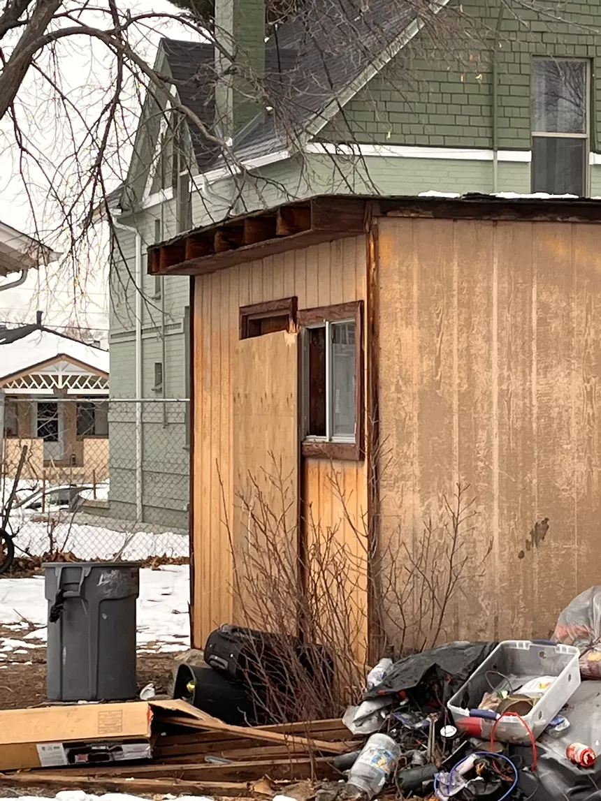 A shed with broken windows and buckets of trash outside.