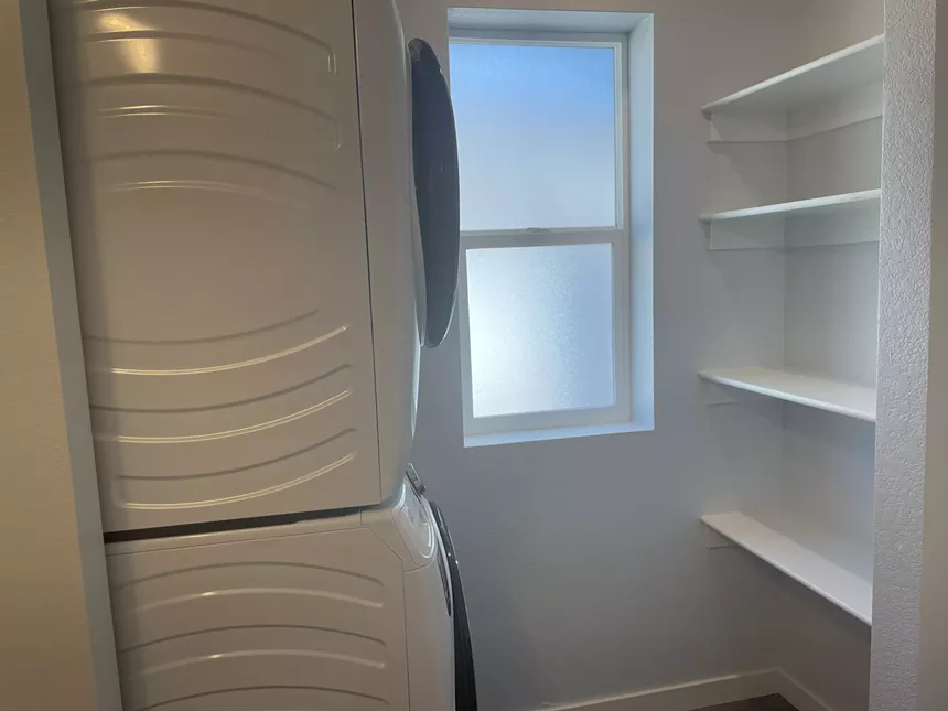 A stacked washer and dryer sits across from built-in shelves.