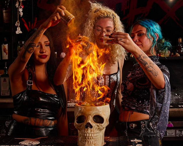 three women behind a cocktail with flames in a skeleton mug