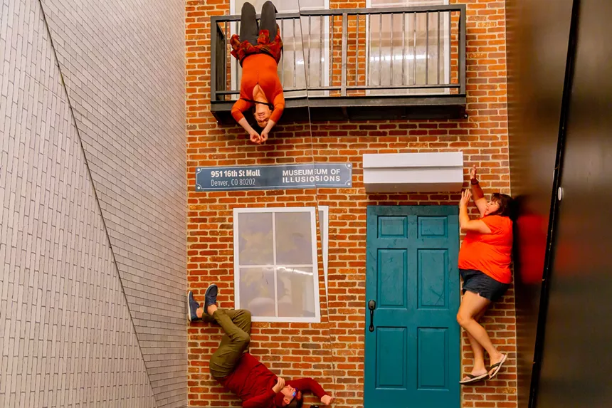 woman hanging off porch of brick townhouse while woman lays to side of door and another in the bottom left corner