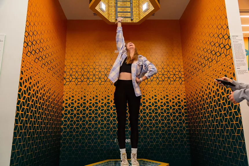 woman in black leggings in orange room has one hand on hip while lifting the other in the air
