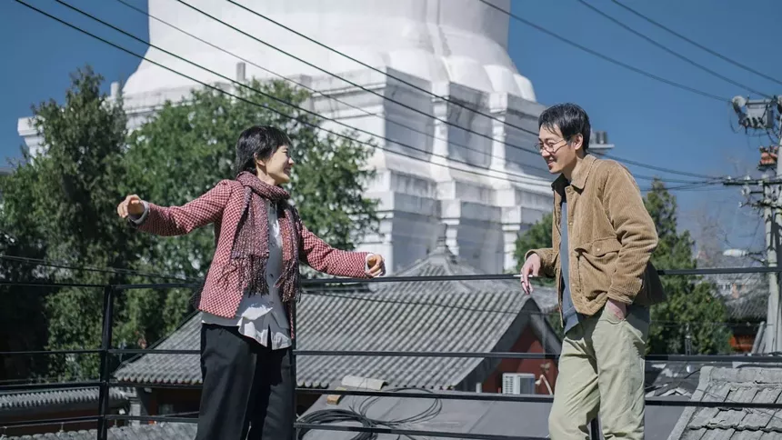 a woman and a man smiling and talking to each other while leaning against a chainlink fence