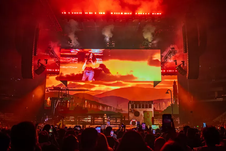 woman performing on stage with screens showing a bright orange sunset