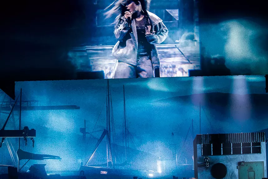 blue lighting on a stage with a screen showing a woman a singing into a mic