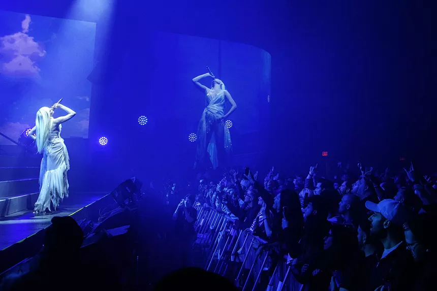 blonde woman singing on stage with blue lights in front of a big audience