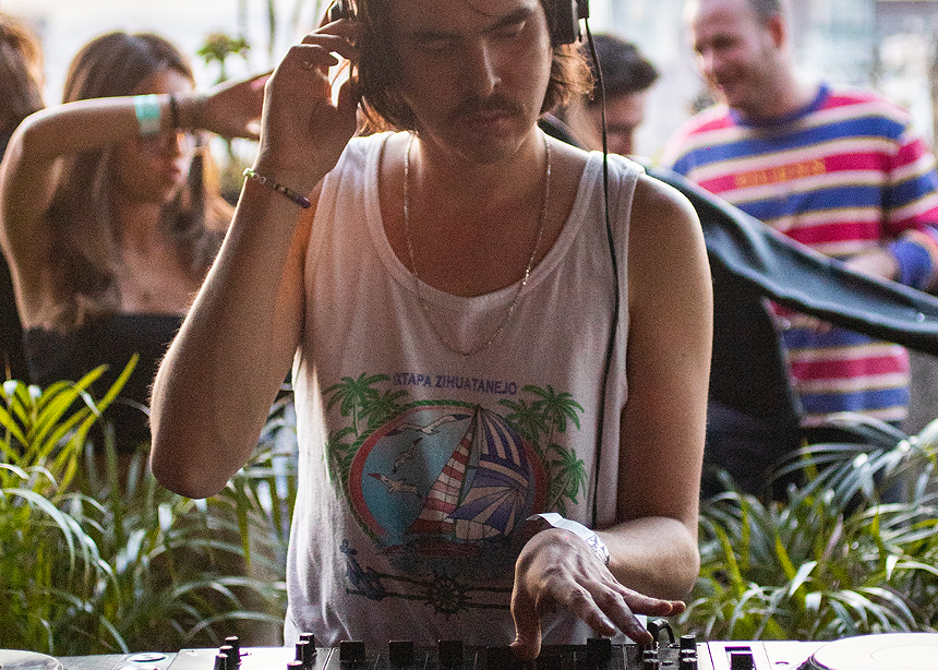 a man in a white tank top deejaying while wearing headphones