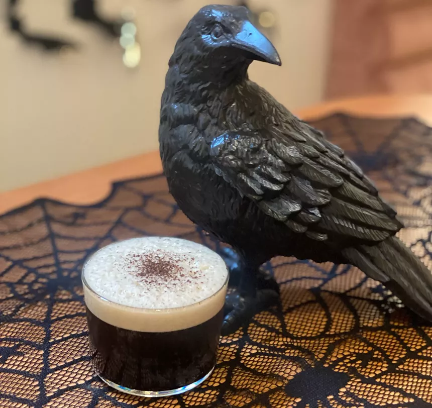 a dark cocktail next to a crow figurine