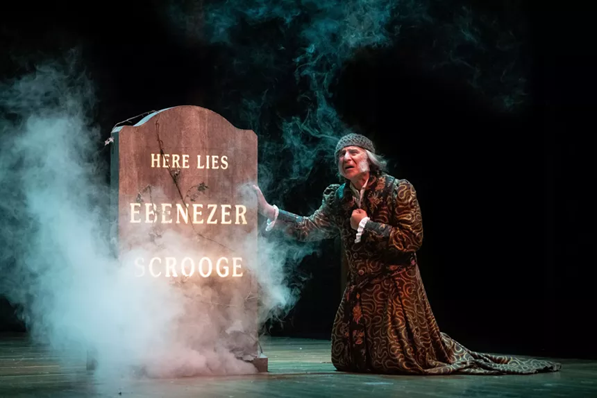 Ebenezer Scrooge kneels in front of his grave