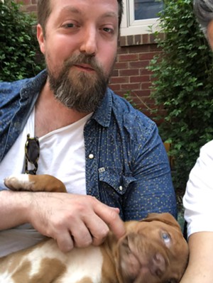 A bearded man pets a brown puppy.