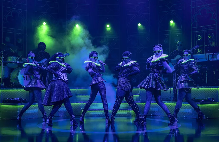 women in medieval costumes pose on stage with microphones under blue lighting
